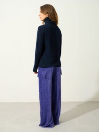 Granatowy sweter z golfem z miękkiego materiału, w zestawie z luźnymi fioletowymi spodniami o szerokich nogawkach z kieszeniami po bokach i pionowymi liniami.