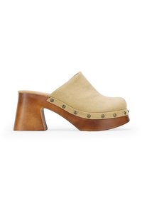 Zuecos de ante beige con punta redondeada, tacón de bloque de madera y tachuelas metálicas a lo largo de la base. Textura suave con un diseño robusto.