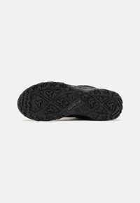 Black outdoor shoe sole with deep treads, featuring a textured rubber surface and recognizable brand logo, designed for traction and durability.