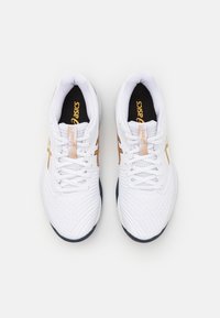 Des baskets blanches de sport avec une tige en mesh respirant, des lacets ton sur ton, des accents dorés et une semelle texturée pour une meilleure adhérence.