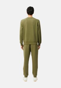 Conjunto de sudadera y pantalones deportivos en verde oliva, confeccionado con tela suave, con puños acanalados y un diseño sencillo, combinado con zapatillas blancas.