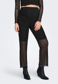 Mustad võrgupüksid läbipaistvate detailidega, millel on õrn täpiline tekstuur. Kantud mustade pahkluu saabastega, rõhutades vormitud disaini.