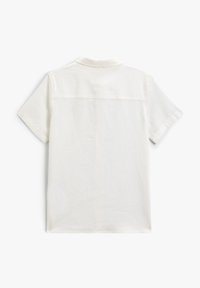 Camisa blanca de manga corta hecha de una tela ligera, con cuello y un detalle de yugo en la parte posterior. Textura suave y diseño simple.