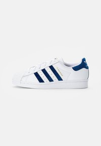 White sneaker featuring blue stripes and accents, textured back heel, rubber sole, and distinctive shell toe design.