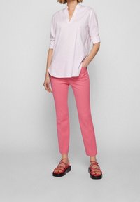 Blouse rose clair à col avec manches courtes ; associée à un pantalon slim rose vif et des sandales rouges à fines brides sur une semelle noire.