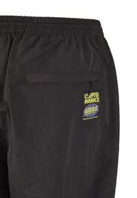 Schwarze Shorts mit elastischem Bund, ausgestattet mit einer Gesäßtasche und einem Clepto Manix-Logo-Patch in Gelb und Blau. Glatte Textur.