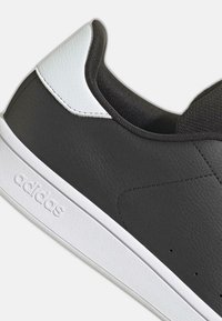 Czarno-białe sneakersy Adidas z teksturowaną skórzaną cholewką, białą podeszwą i wyściełanym czarnym kołnierzem, ukazane z boku.