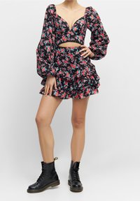 Černý květinový crop top s volnými rukávy a hlubokým V výstřihem, v kombinaci s volánkovou mini sukní. Oblečeno s černými šněrovacími vojenskými botami.