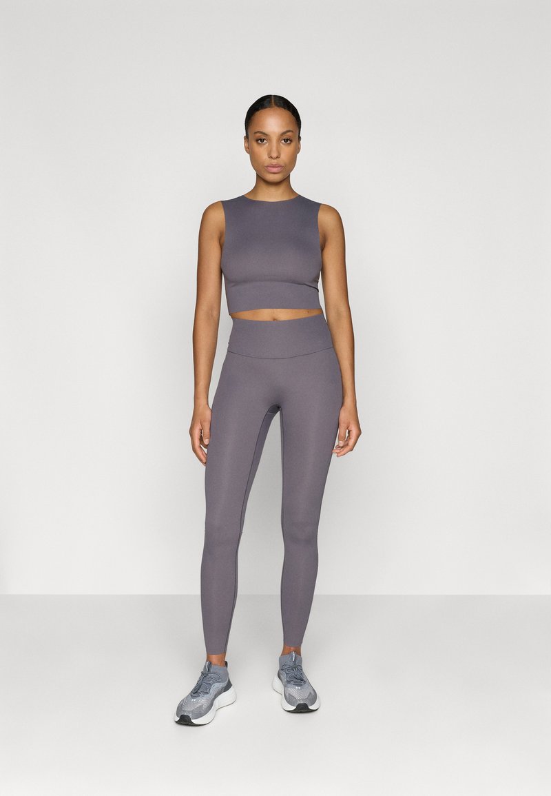 Conjunto de ropa deportiva gris que incluye un top corto sin mangas y leggings de cintura alta. El material parece suave con un diseño ajustado. Combinado con zapatillas grises.