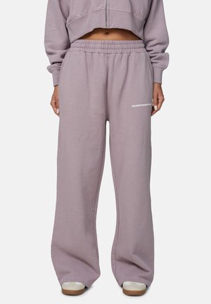 Osoba nosząca luźne, malwowe spodnie dresowe z elastycznym pasem i białe trampki, widoczna krótka, dopasowana malwowa bluza z kapturem odsłaniająca brzuch.