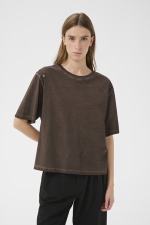 Hnědé oversized tričko z měkké tkaniny, s kulatým výstřihem a krátkými rukávy s kovovými knoflíky u ramene.