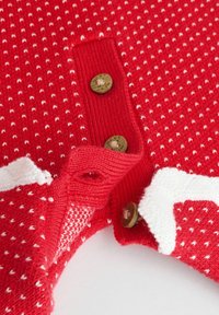Roter Strickpullover mit weißen Musterakzenten, Holzknöpfen, geripptem Kragen und strukturiertem Stoff mit kleinen weißen Punkten.
