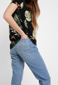 Maglietta nera con motivo floreale verde e arancione, abbinata a jeans in denim blu chiaro con taglio dritto e tasche posteriori.
