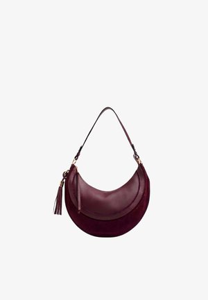 Sac d’épaule rouge foncé en forme de croissant avec un pompon en cuir et une bandoulière réglable sur fond blanc.