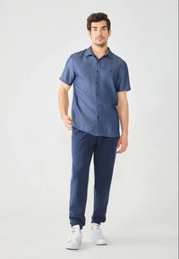 Kortærmet, marineblå stribet skjorte med knaplukning. Kombineret med mørkeblå tapered bukser og hvide sneakers. Glatte teksturer hele vejen igennem.