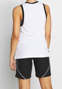 Biały siatkowy tank top sportowy z czarnymi wykończeniami, zestawiony z czarnymi szortami z białymi akcentami. Skoncentrowany na sportowym designie i wygodnym dopasowaniu.