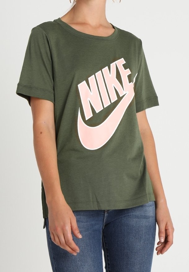 Olivgrön bomull t-shirt med en stor rosa Nike-logotyp. Korta ärmar med uppvikta manschetter och en avslappnad passform.