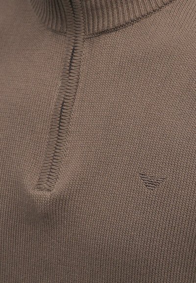 Pull en maille marron avec un col haut et une courte fermeture éclair. Présente une texture côtelée et un logo discret en bas à droite.