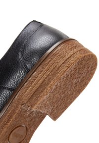 Scarpa in pelle nera con superficie testurizzata, caratterizzata da una suola in gomma marrone spessa con dettagli scanalati e tacco arrotondato.