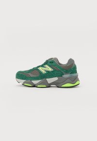 Zöld velúr és hálós sneaker, szürke középtalppal, fényvisszaverő díszítésekkel, és élénk zöld talppal, amely textúrázott részleteket tartalmaz.