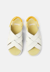 Hvide sandaler med krydsede stropper og gule detaljer. Har en polstret indersål og en gummisål for godt greb. Minimalistisk design.