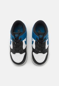 Vita och svarta sneakers med blå accenter, med en perforerad tå, rund snörning och en vadderad krage för komfort. Nike-logotypen är synlig.