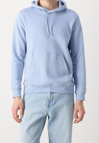 Světle modrá mikina s kapucí z měkké látky, s přední kapsou, kapucí se stahovací šňůrkou a decentním logem na hrudi. Standardní střih, žebrované manžety.