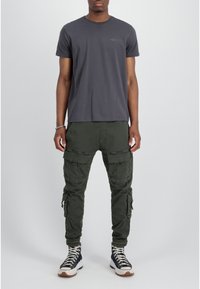 Camiseta de algodón gris oscuro con mangas cortas y cuello redondo, combinada con pantalones cargo verde oliva que cuentan con múltiples bolsillos y cremalleras.