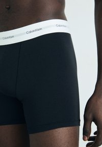 Boxer da uomo in cotone nero con un elastico bianco in vita che presenta il marchio "Calvin Klein". Texture liscia e design aderente.