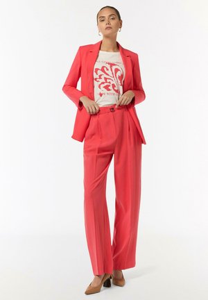 Coral suit with a fitted blazer and wide-leg trousers, paired with a light graphic t-shirt. Includes brown heels and a buckle detail.