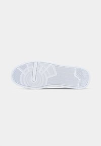 Sohle eines weißen Sneakers mit gemusterten Rillen und "Tommy Hilfiger" in der Mitte des kreisförmigen Designs eingeprägt.