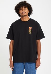 Black cotton T-shirt featuring a front graphic in orange, yellow, and black. Short sleeves and a crew neckline. Relaxed fit.