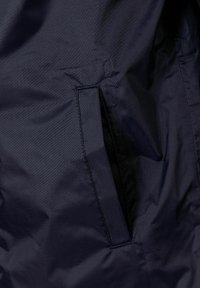 Tummansininen kevyt takki, jossa on sivutasku, sileä matta pintatekstuuri ja hienovaraiset ompeluyksityiskohdat.