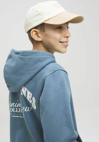 Felpa in cotone blu dal tocco morbido, con cappuccio e lettering bianco sulla parte posteriore. Un berretto beige con visiera chiara completa il look.