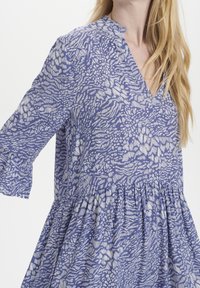 Abito blu con motivo, scollatura a V e maniche a campana a 3/4. Realizzato in tessuto leggero, presenta una vita arricciata e una gonna fluente.