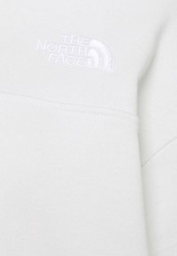 Sudadera gris clara con logo bordado blanco en el pecho. Textura suave, mangas largas y diseño de cuello redondo. Detalles de costura simples visibles.