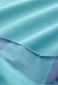 Textile in varying shades of aqua blue and light purple, featuring smooth texture and subtle folds, demonstrating a layered design.