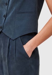 Donkerblauwe linnen vest met hoge kraag, éénrijige knopen en zijzak. Gladde textuur met subtiele glans en een getailleerde pasvorm.