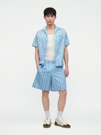 Homme portant une chemise à manches courtes rayée bleu clair et un short assorti, un débardeur blanc, des chaussettes blanches et des baskets bicolores, debout face à l'avant.