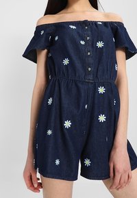 Denim off-shoulder romper with short legs, dark wash, button front, and white daisy embroidery throughout. Elastic waist for fit adjustment.