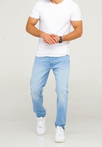 Ljusblå denimjeans med rak passform, bärs med en vanlig vit t-shirt och vita sneakers, vilket visar en avslappnad stil och passform.