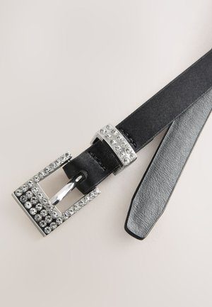 Curea neagră din piele cu o cataramă argintie împodobită cu cristale transparente, având o parte inferioară texturată gri și un design elegant, subțire.