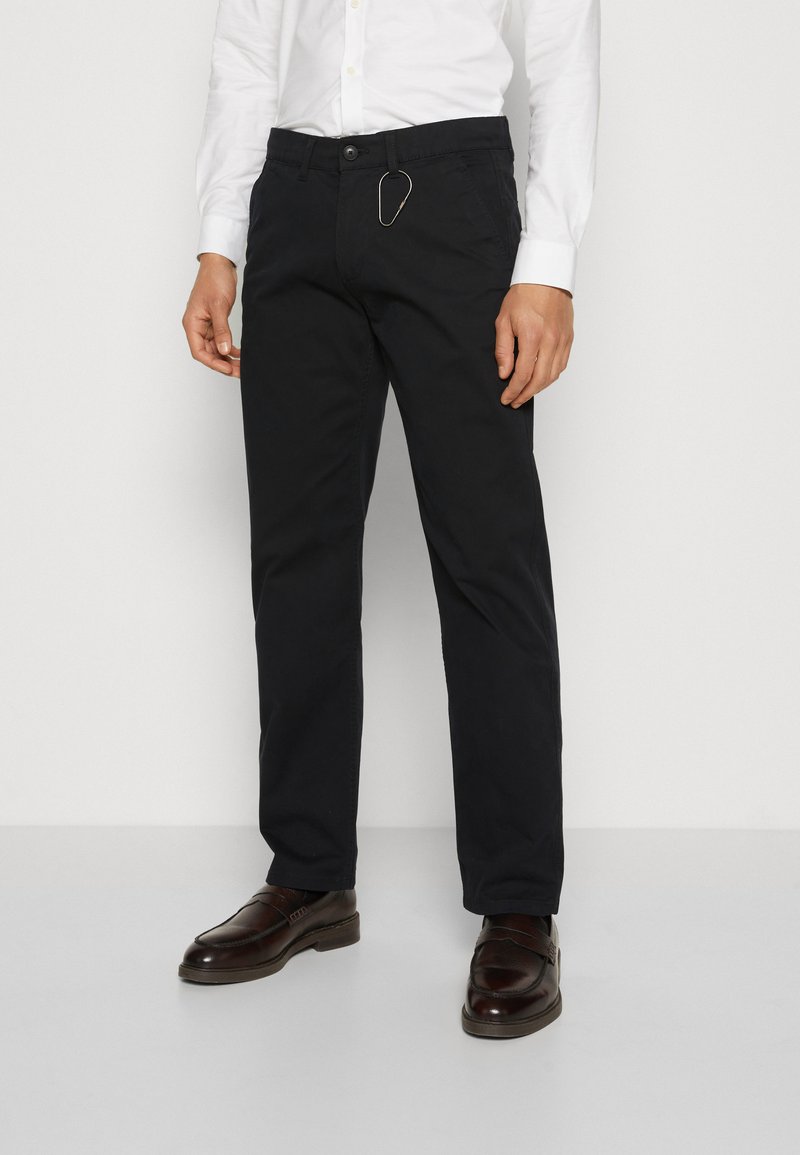 Chinos navy en tissu sergé de coton, avec une coupe standard, des passants de ceinture et un accent de porte-clés en or décoratif. Associés à des chaussures marron.