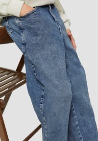 Lichtblauwe denim jeans met een relaxte pasvorm, voorzien van zijzakken en zichtbare stiksels, gecombineerd met een sweatshirt in een neutrale kleur.