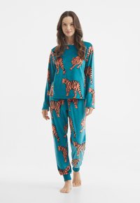 Conjunto de pijama turquesa en tela suave con un estampado de tigre naranja. Parte superior de manga larga combinada con pantalones ajustados, ambos con puños acanalados.
