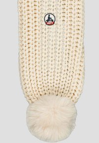 Crème gebreide sjaal met losse, dikke steken, een ronde bontachtige pompon aan één uiteinde en een ronde logopatch met de tekst "JOTT."