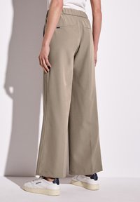 Breda byxor i khaki-tyg med elastisk midja och sidofickor. Slät textur, kombinerat med vita sneakers med marinblå accenter.