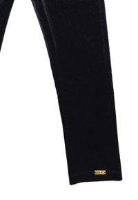 Leggings neri elasticizzati realizzati in un morbido materiale vellutato. Presentano un piccolo logo dorato sull'orlo e un design aderente.