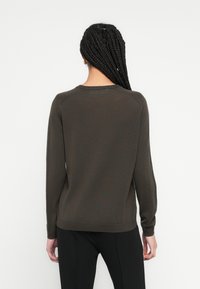 Chaki spalvos megztinis su apvalia iškirpte ir ilgomis rankovėmis; pasižymi lygiu mezgimo raštu ir briaunuotu apačios kraštu. Dėvimas su juodomis kelnėmis.