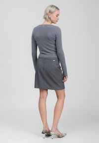 Maglione grigio a maglia con un design aderente, abbinato a una gonna grigia con righe sottili e piccoli pois bianchi. Tacchi leggeri a fantasia.